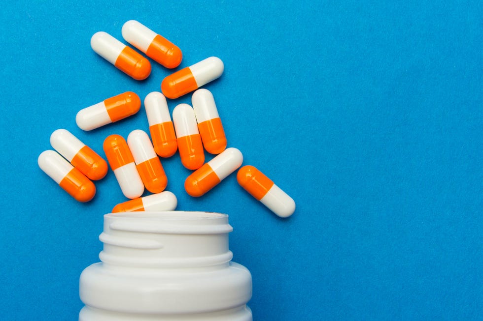 Orange white capsules (pills) were poured from a white bottle on a blue background. Medical background, template. orange white capsules pills were poured from a white bottle on a blue background medical background, template