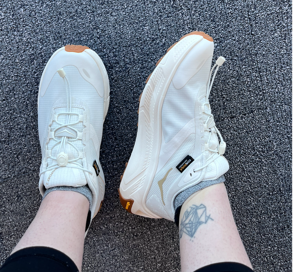 White athletic shoes worn by a person with a tattoo on their ankle.